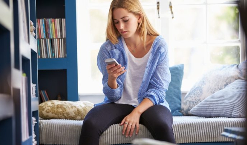 la femme est assise sur le lit avec le telephone a la main