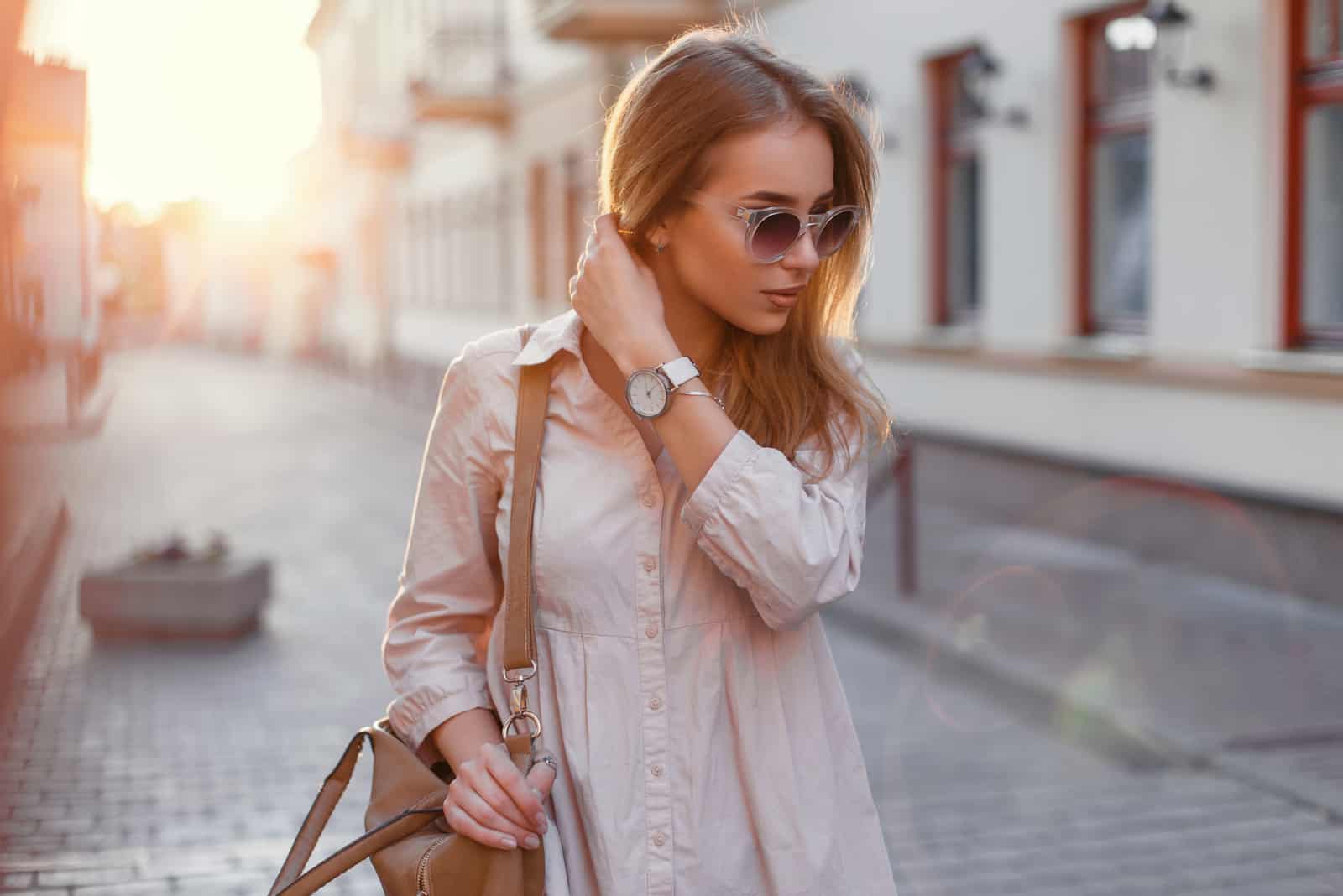 Jeune belle fille dans des lunettes de soleil élégantes et avec un sac à la mode au coucher du soleil.
