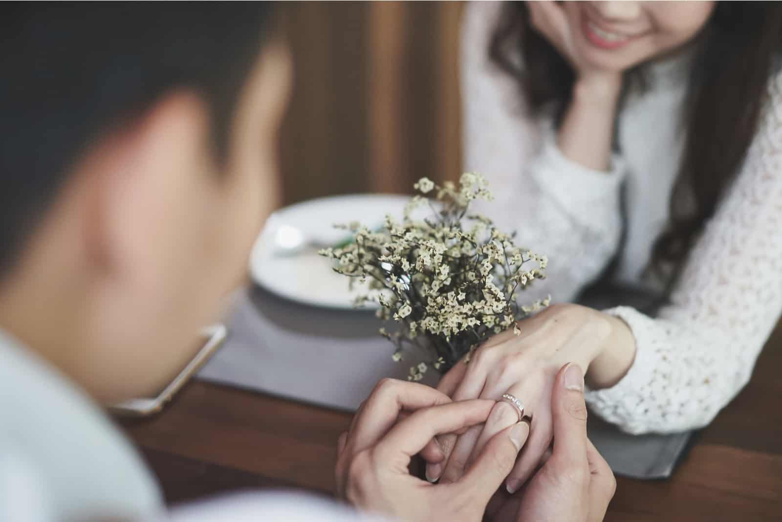 La main du jeune homme tenant une bague de fiançailles en diamant en argent pour la proposition à une jeune femme