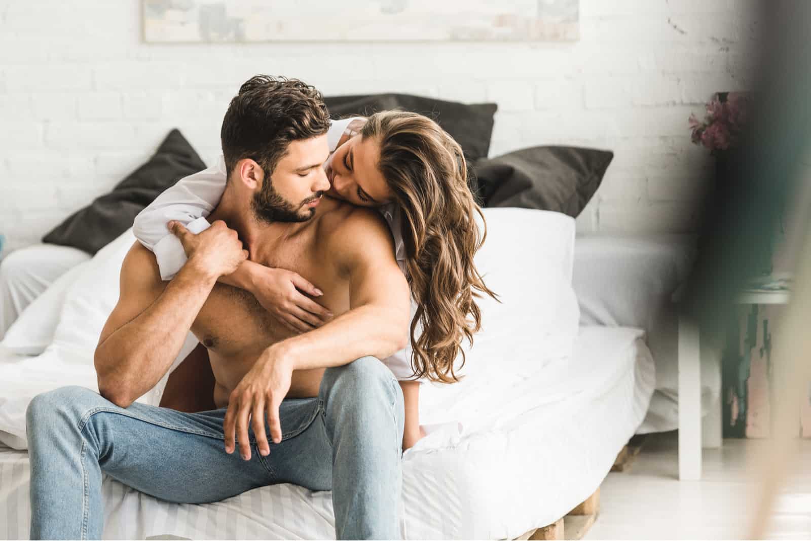 la femme a serré l'homme dans ses bras alors qu'il était assis sur le lit et l'a embrassé sur la joue