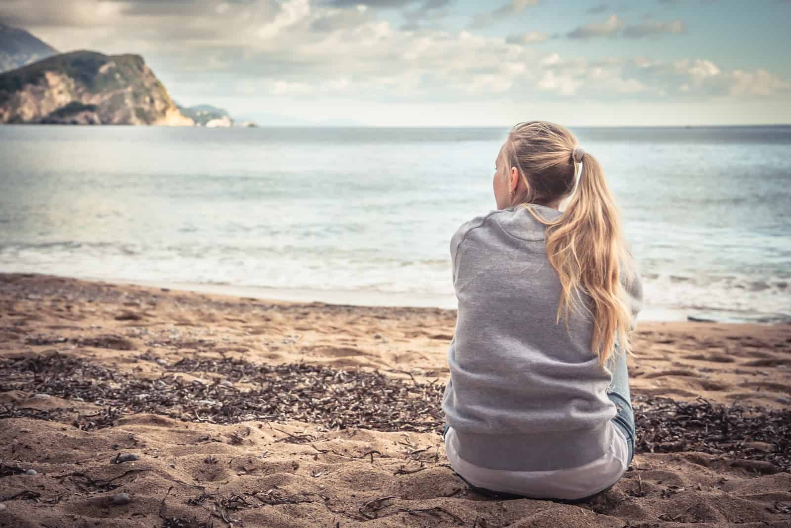 femme assise sur la plage serrant ses genoux