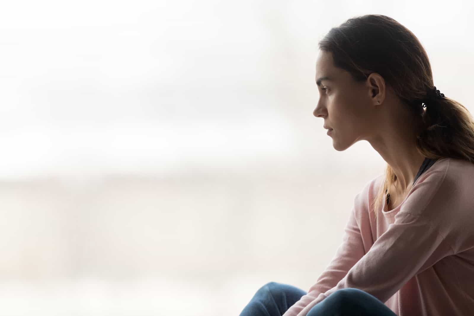 fille pensive assise seule regardant à travers la fenêtre