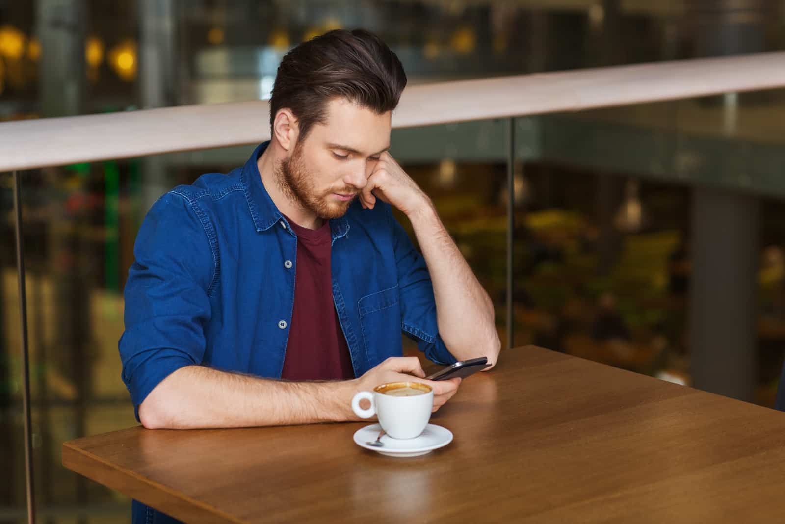 un homme assis à une table de boire du café et en appuyant sur un téléphone