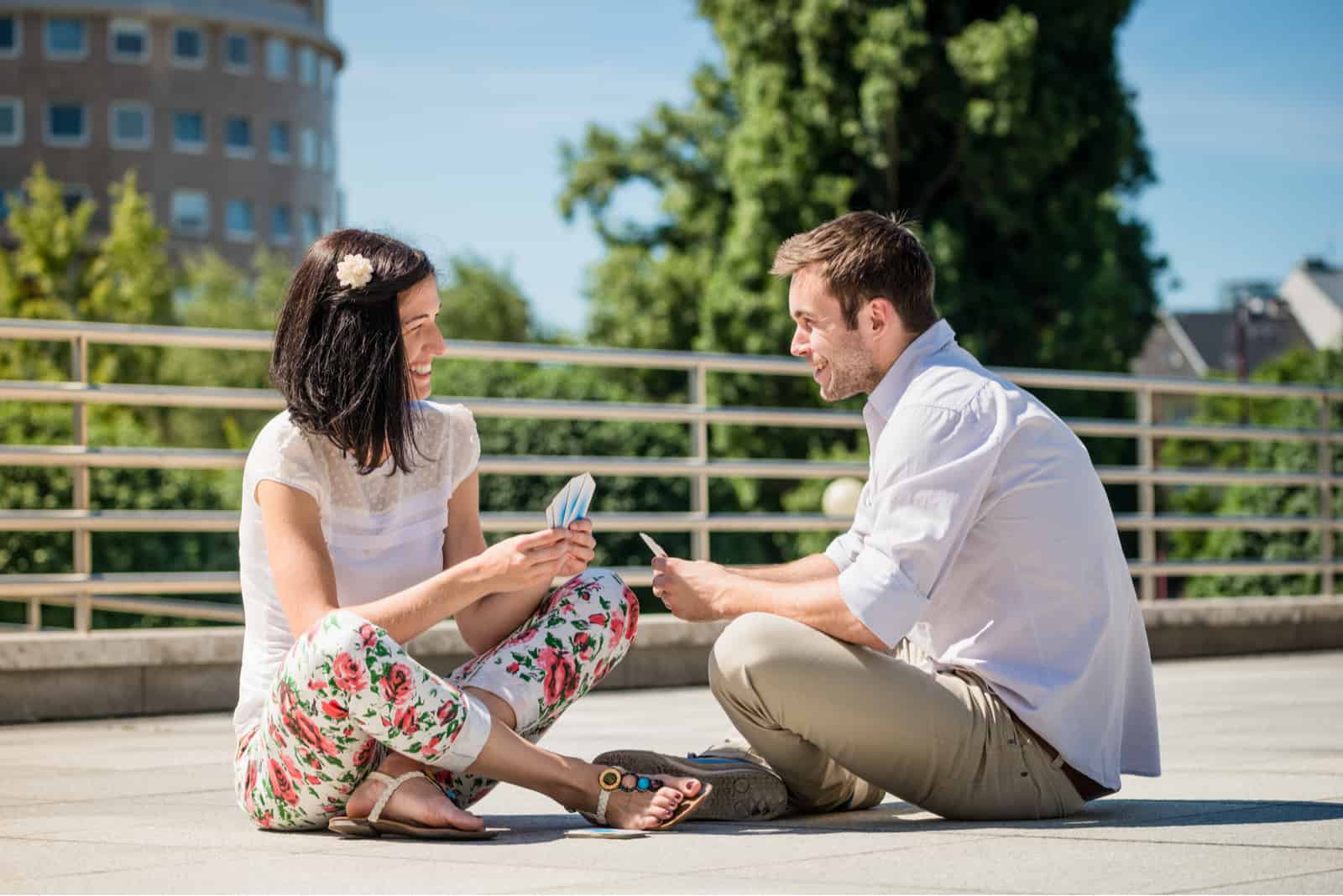 un homme et une femme s'assoient sur le béton et jouent aux cartes
