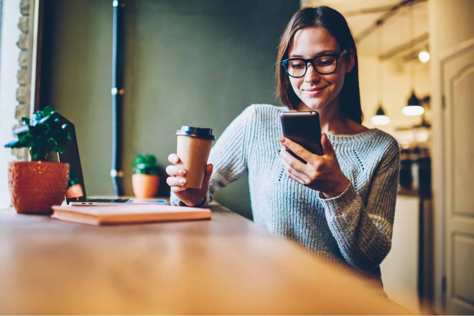une femme assise avec du café tenant un téléphone dans sa main