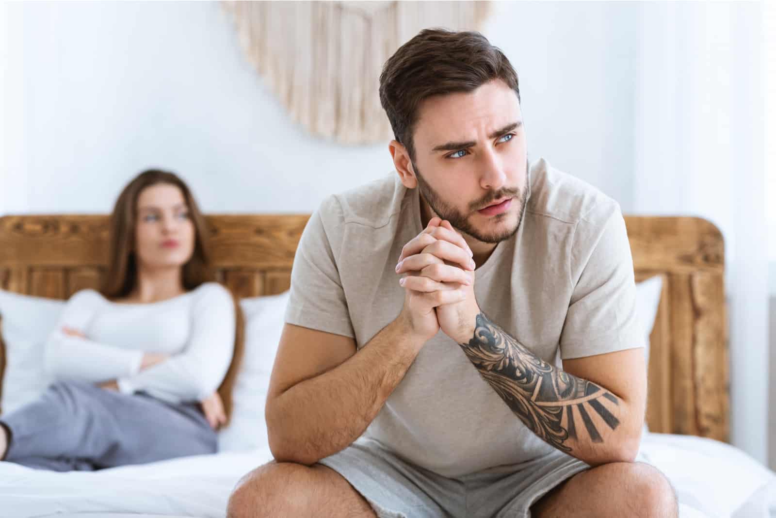 une femme en colère se trouve sur le lit tandis qu'un homme pensif est assis