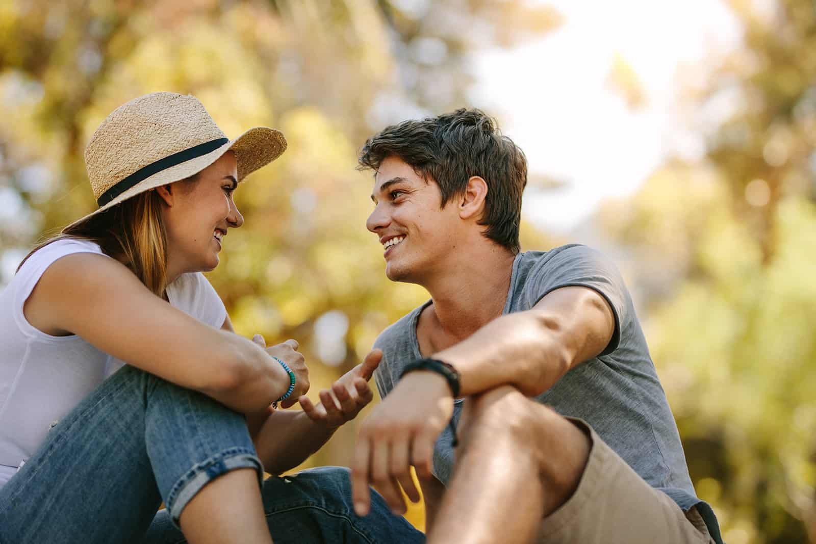 Couple souriant assis à l'extérieur en se regardant et en parlant dans le parc