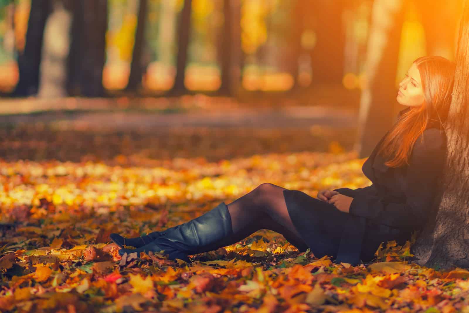 Femme en manteau noir et bottes en cuir assis sous l'arbre