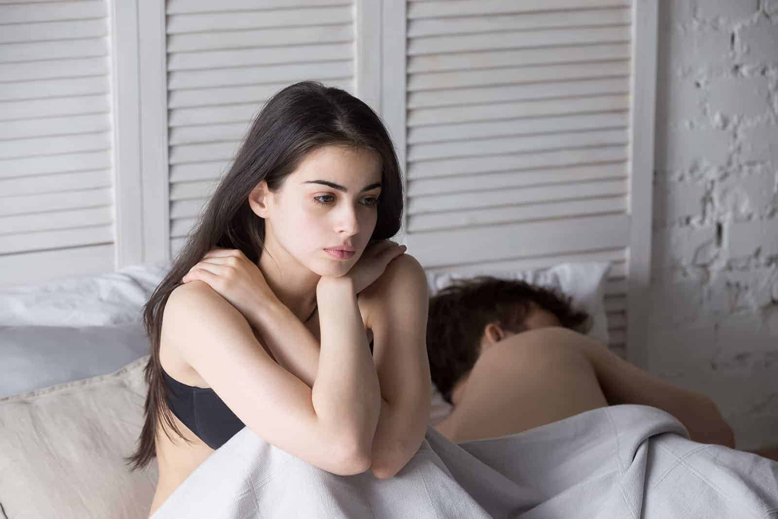 Triste femme frustrée assise dans le lit à côté d'un homme endormi