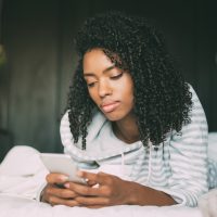 Une femme sérieuse aux cheveux bouclés à l'aide de smartphone sur le lit