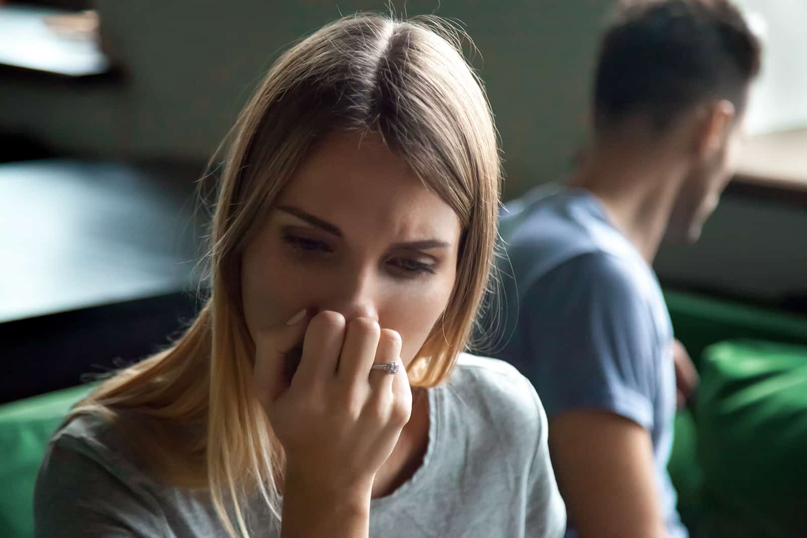 Une femme frustrée assise séparée sur le canapé avec l'homme à la maison, couvrant le visage avec la main