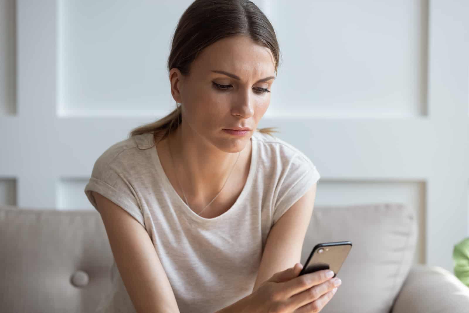 malheureuse femme réfléchie regardant l'écran du téléphone portable