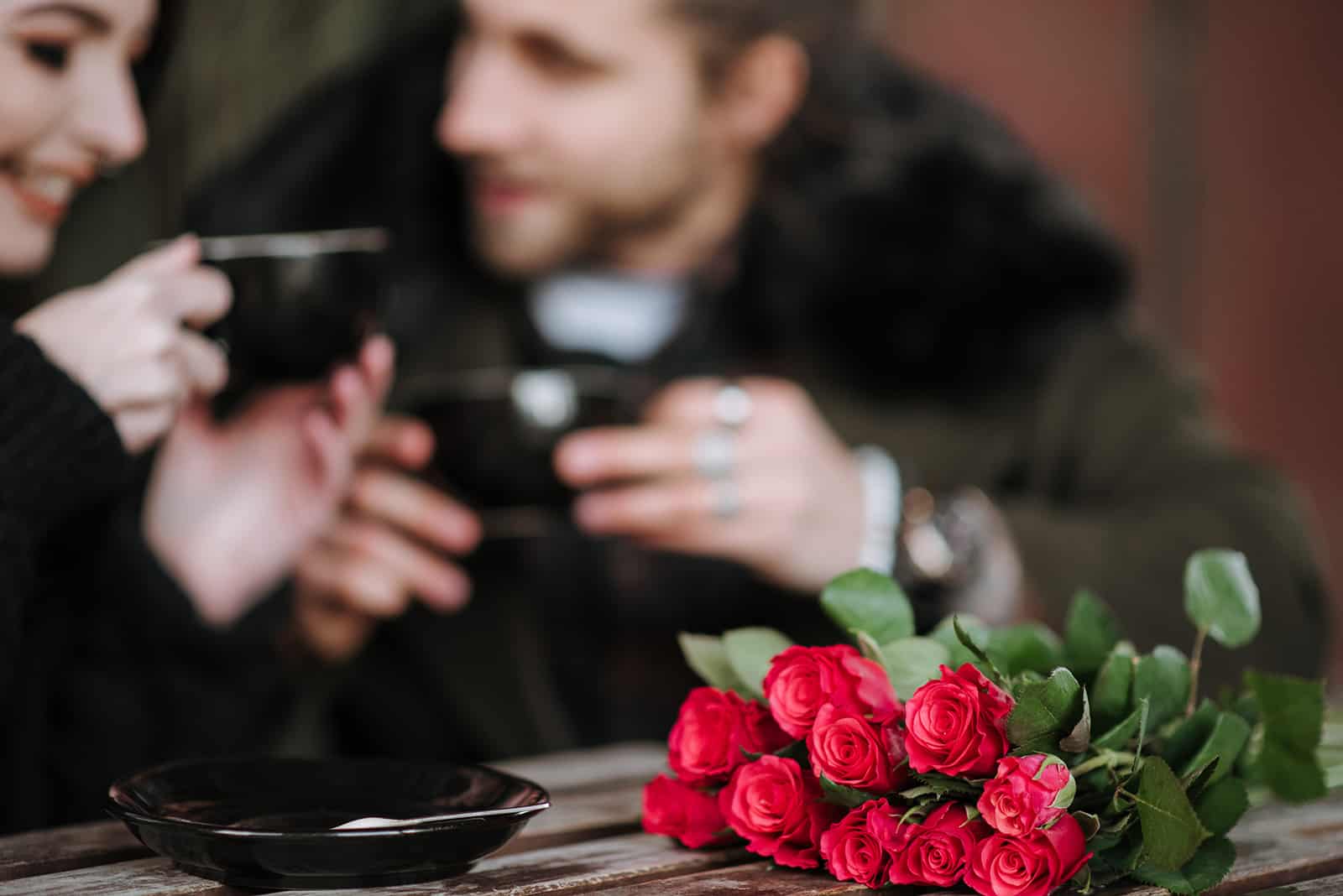 roses rouges sur une table devant couple buvant du café