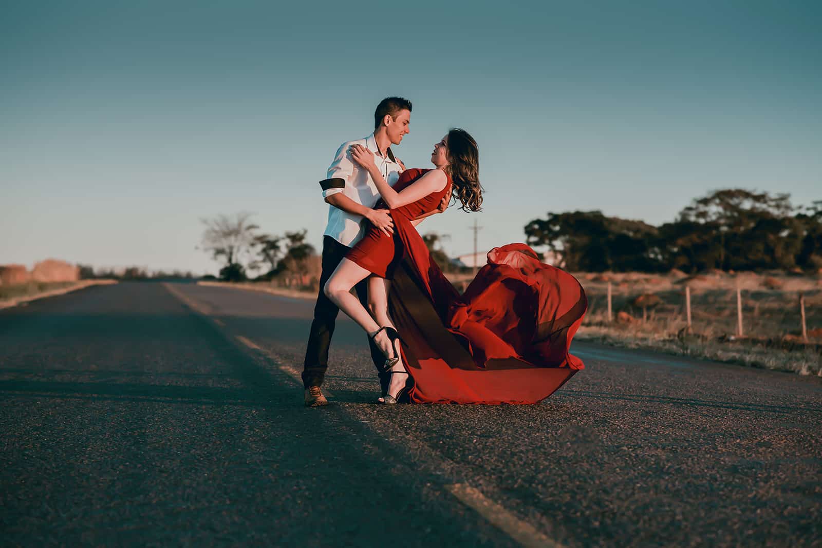 un homme dansant avec une femme en robe élégante rouge sur une route