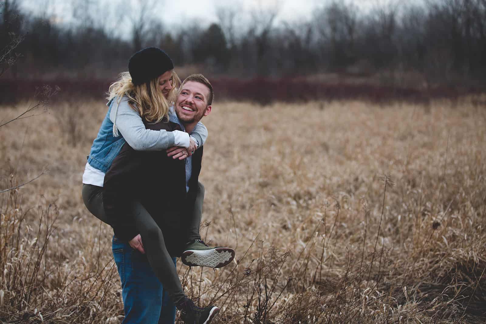 un homme souriant portant une femme sur le dos à travers le champ