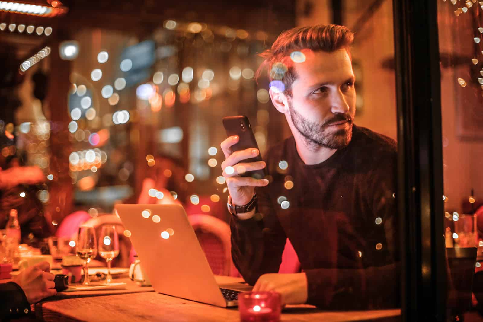 un homme tenant un smartphone dans un restaurant et regardant par la fenêtre