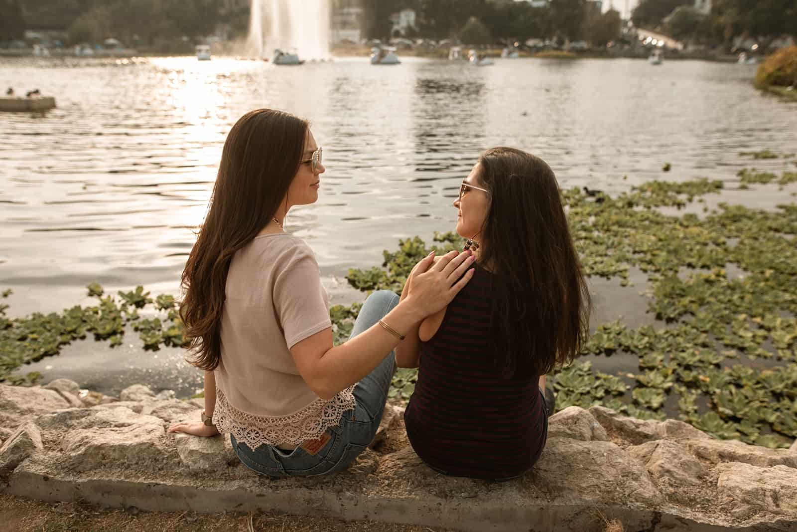 Une femme encourageant son amie alors qu'elle était assise ensemble près du lac