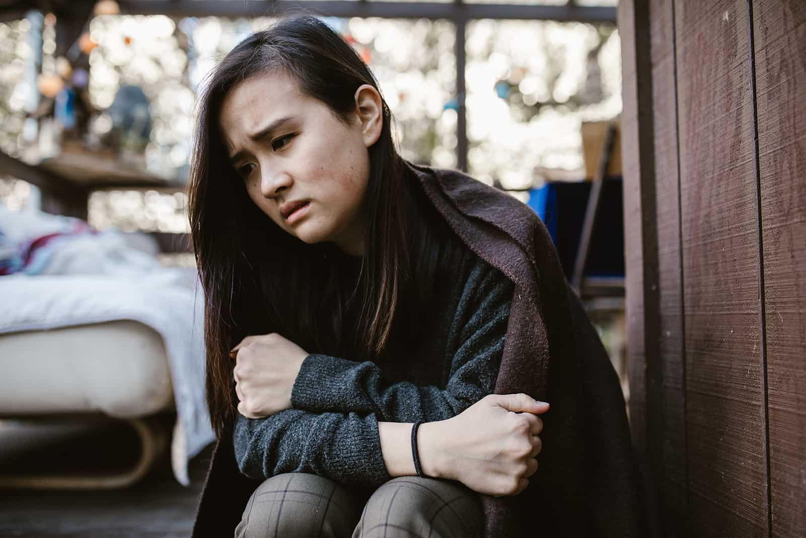 une femme triste couverte de couverture assise sur la terrasse