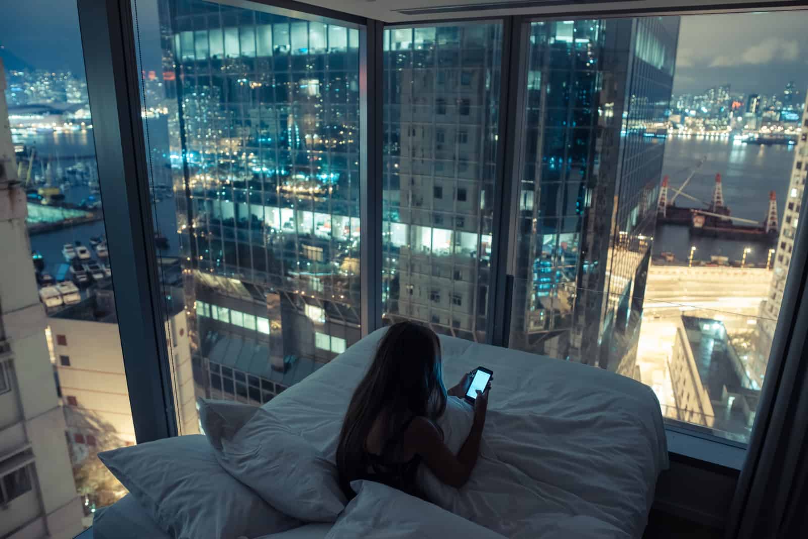 femme assise dans son lit et clé sur le téléphone