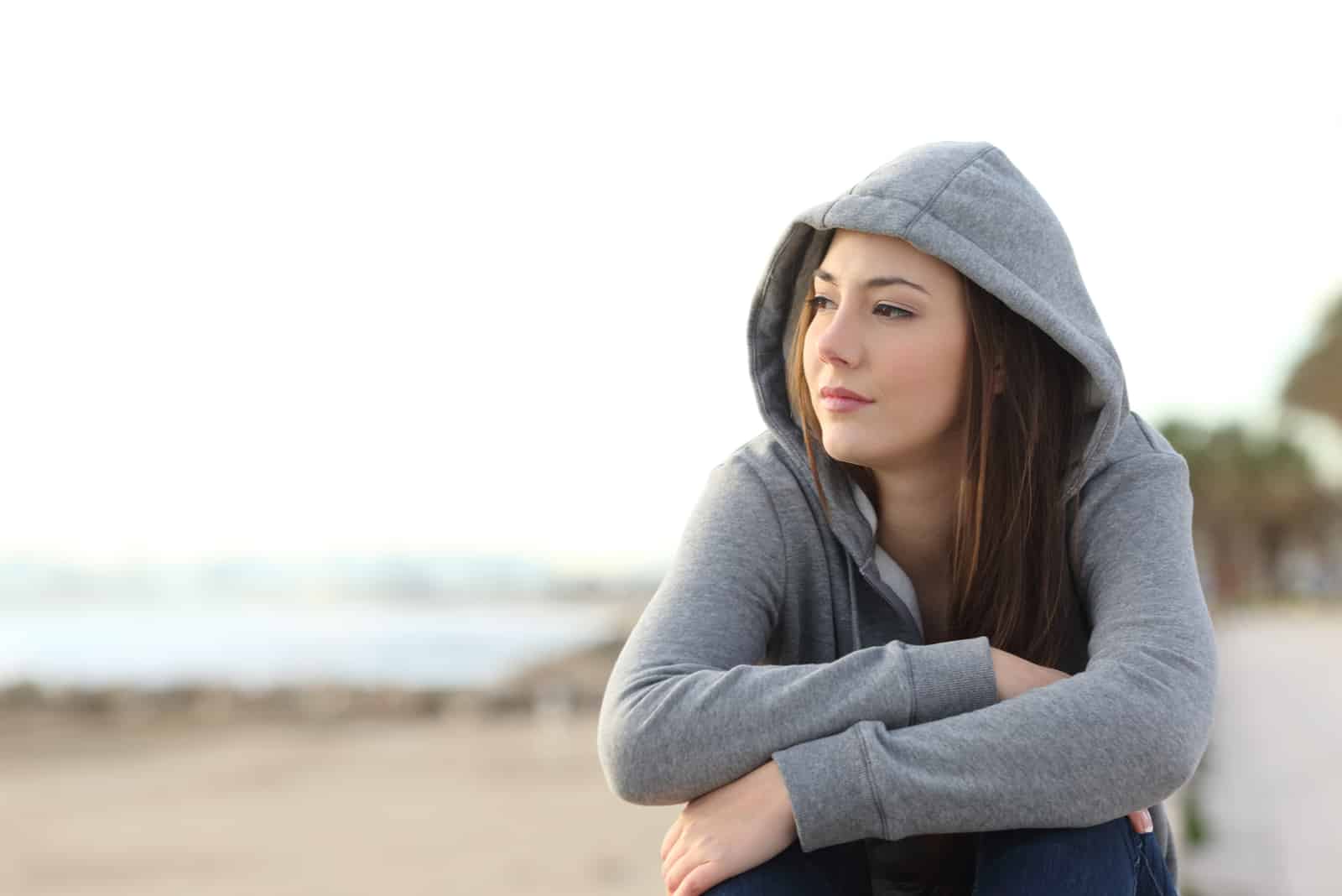 Adolescent pensif assis sur la plage à lécart