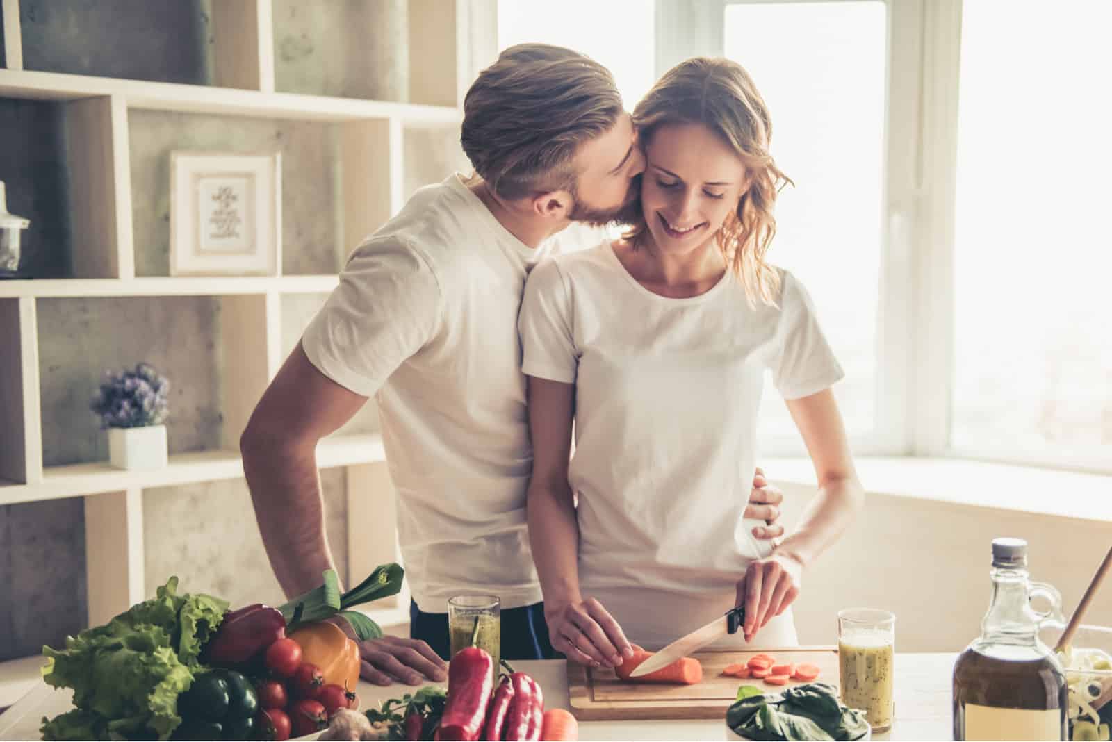 Beau jeune couple parle et souriant tout en cuisinant des aliments sains dans la cuisine à la maison