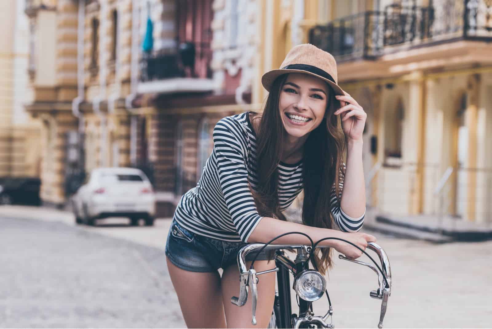 Belle jeune femme se penchant sur son vélo et souriant tout en se tenant à l'extérieur