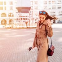 Enthousiaste à la mode jeune femme tenant un café en plein air marchant dans la rue