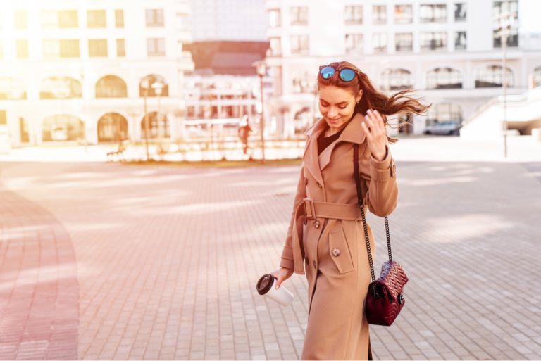 Enthousiaste à la mode jeune femme tenant un café en plein air marchant dans la rue