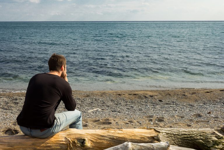 un homme est assis et regarde la mer