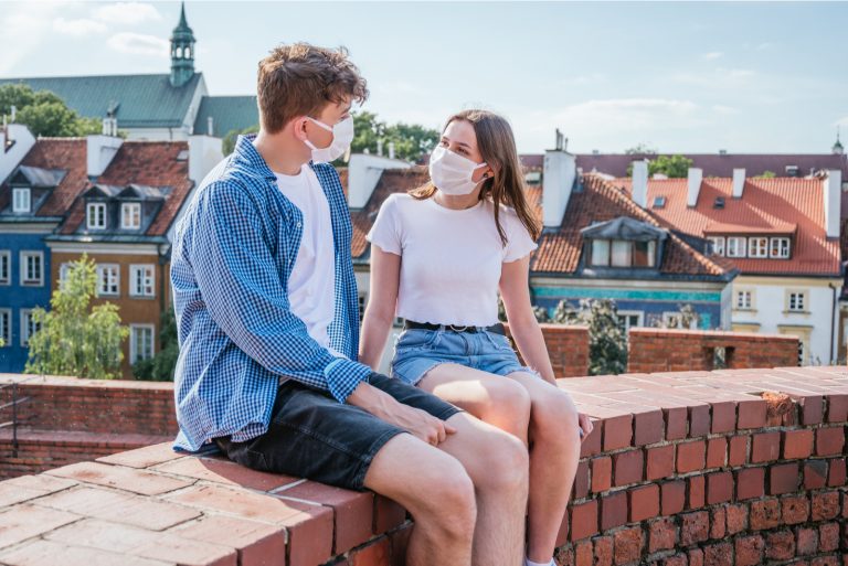 un homme et une femme avec des masques s'assoient sur le mur et parlent