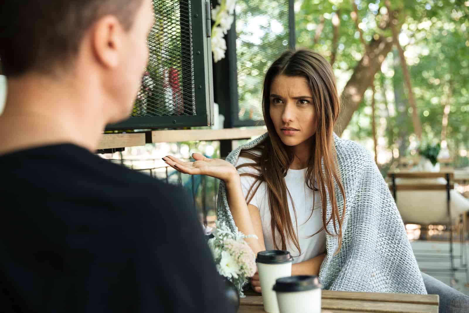Confus jeune femme faisant des gestes avec la main et regardant son petit ami alors qu'il était assis dans un café dans le parc en plein air