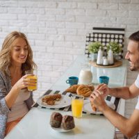 un homme et une femme assis à une table en riant tout en prenant le petit déjeuner