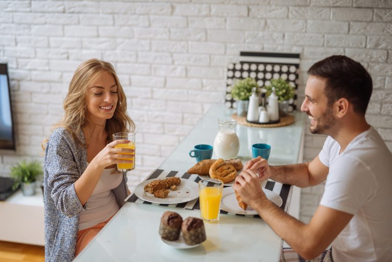 un homme et une femme assis à une table en riant tout en prenant le petit déjeuner