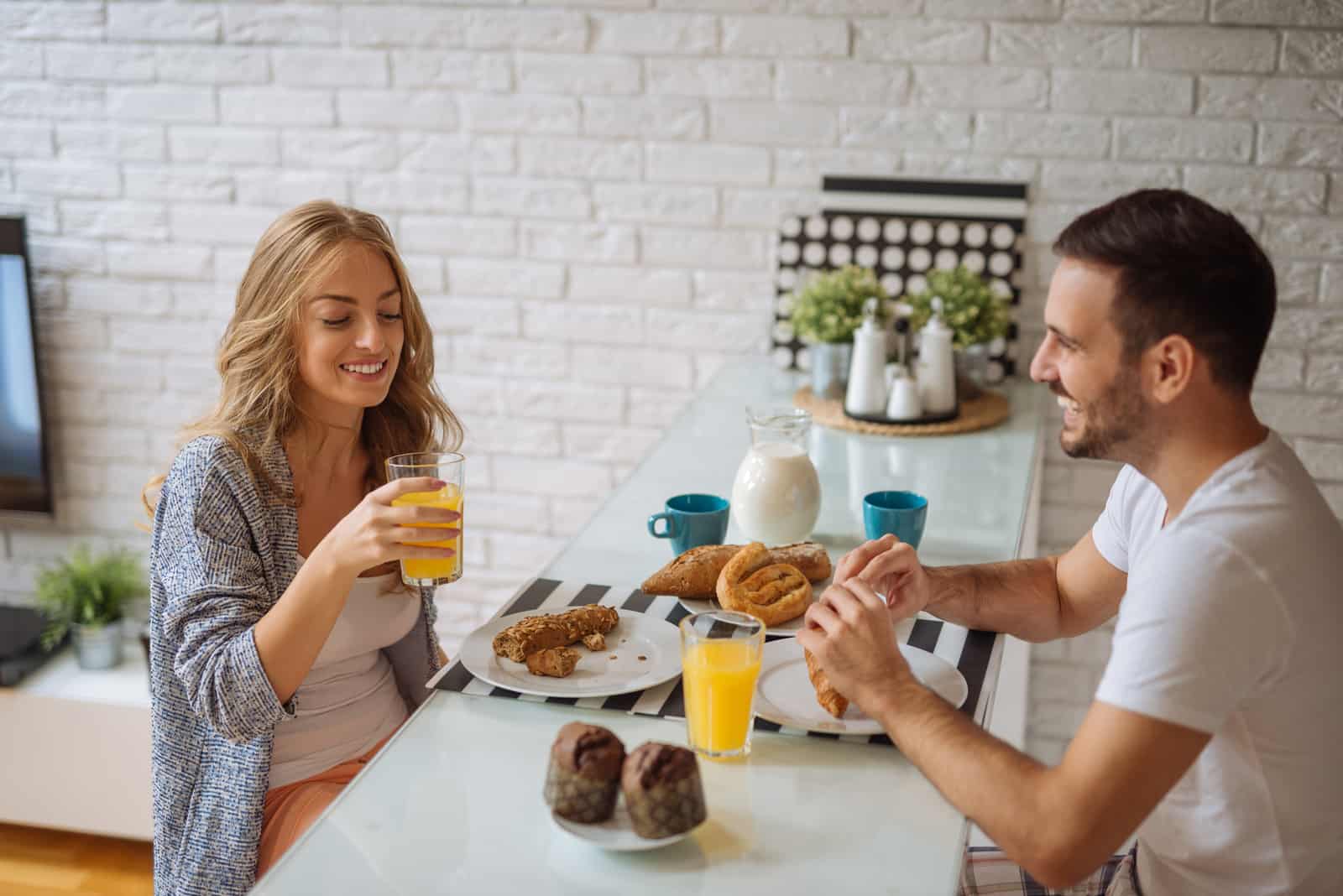 un homme et une femme assis à une table en riant tout en prenant le petit déjeuner