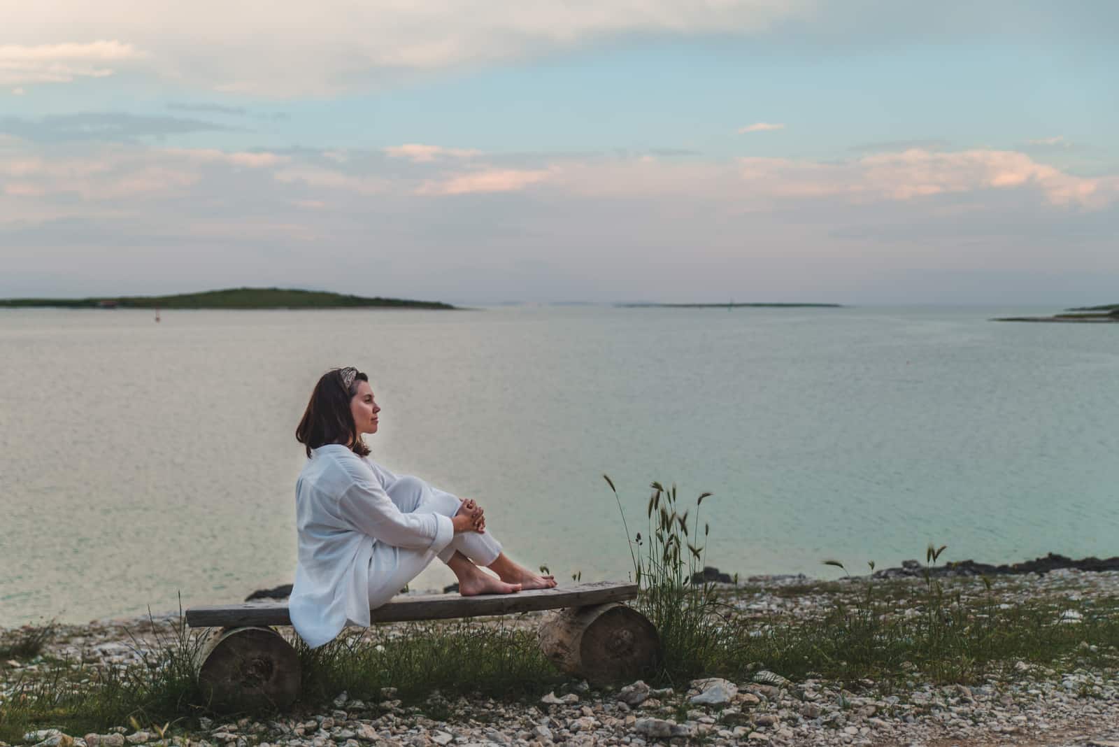Femme assise sur un banc à la recherche sur le coucher du soleil sur la mer