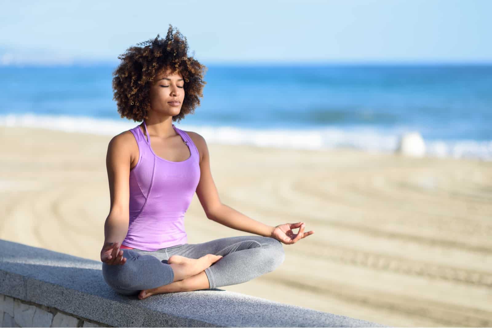 Femme noire, coiffure afro, faisant du yoga asana sur la plage avec les yeux fermés