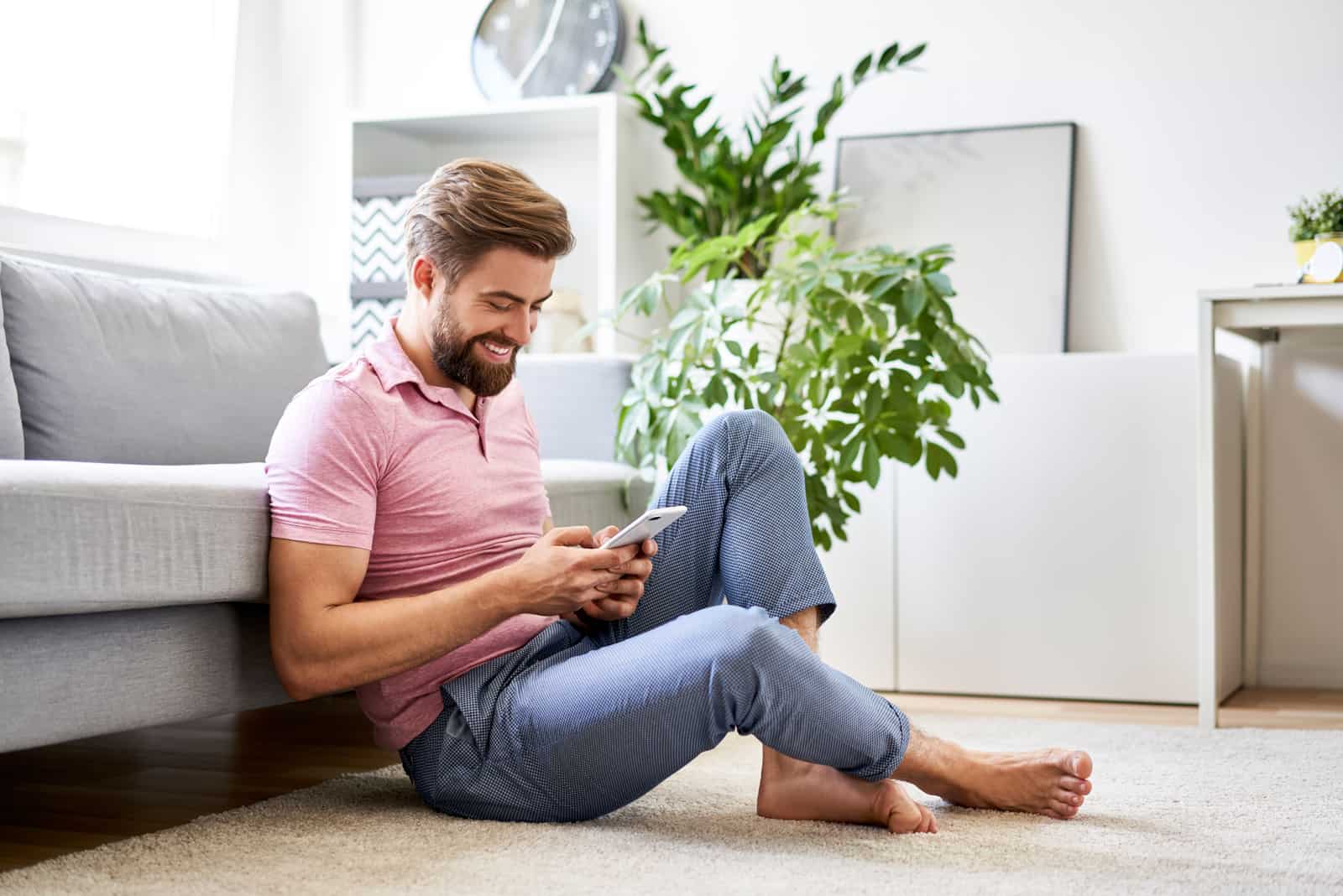 Homme heureux et détendu à la maison à l'aide de téléphone assis sur le sol