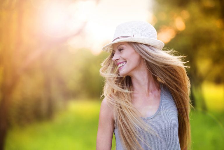 Une femme aux longs cheveux blonds avec un chapeau sur la tête rit