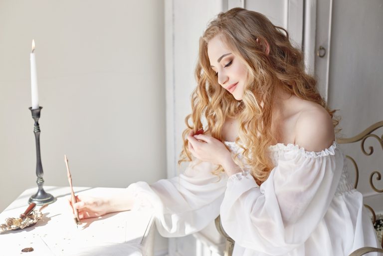 une femme aux longs cheveux blonds est assise et écrit une lettre