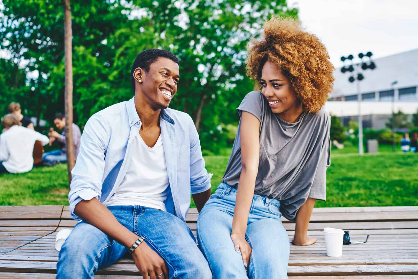 Positif jeune homme afro-américain flirter avec petite amie attrayante à la peau sombre timide pendant la date en milieu urbain