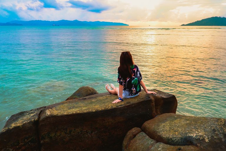 Une jeune femme aux longs cheveux noirs est assise sur un rocher et donne sur la mer