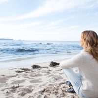 une jeune femme est assise sur la plage et donne sur la mer