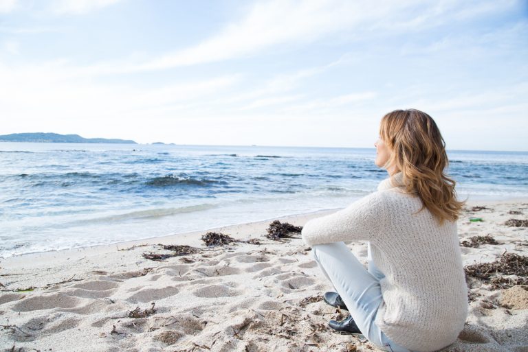 une jeune femme est assise sur la plage et donne sur la mer