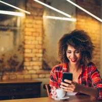Jeune femme au café de boire du café et à l'aide de téléphone mobile