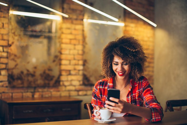 Jeune femme au café de boire du café et à l'aide de téléphone mobile