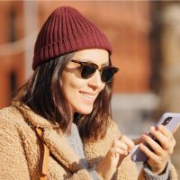 une femme souriante avec un chapeau bordeaux se dresse et un bouton sur le téléphone