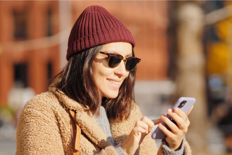 une femme souriante avec un chapeau bordeaux se dresse et un bouton sur le téléphone