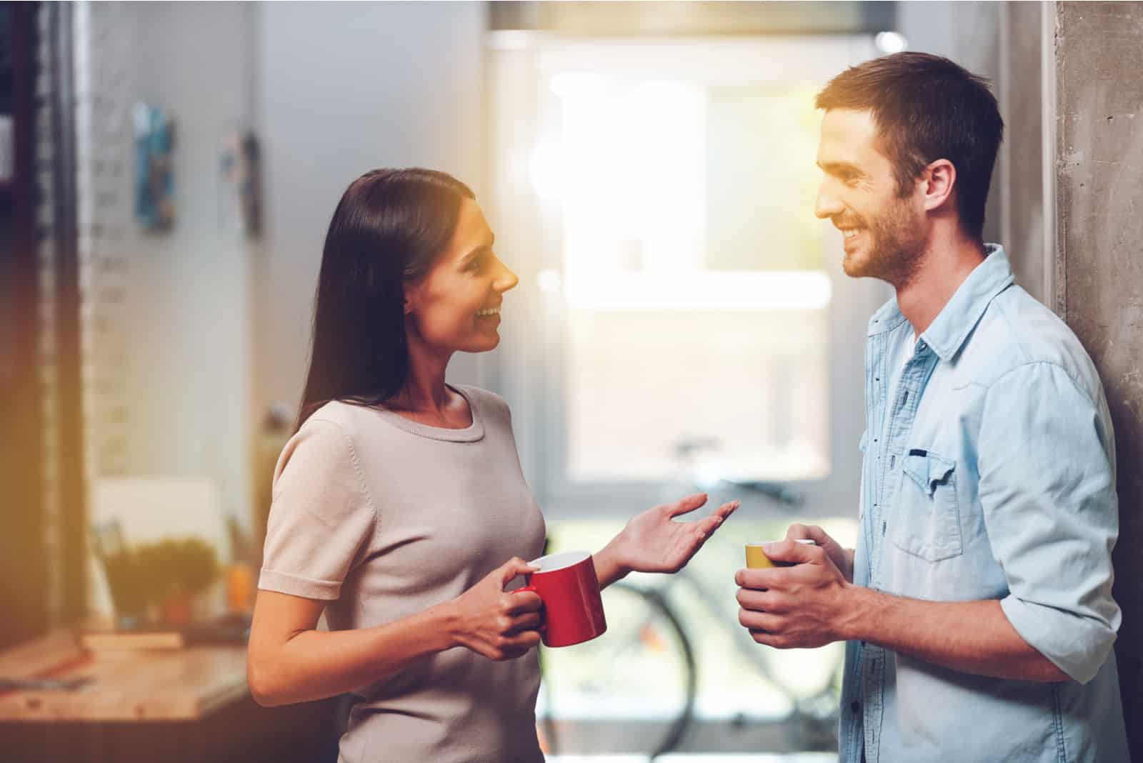 Un homme et une femme souriants se tiennent debout et parlent tout en tenant des tasses de café dans leurs mains