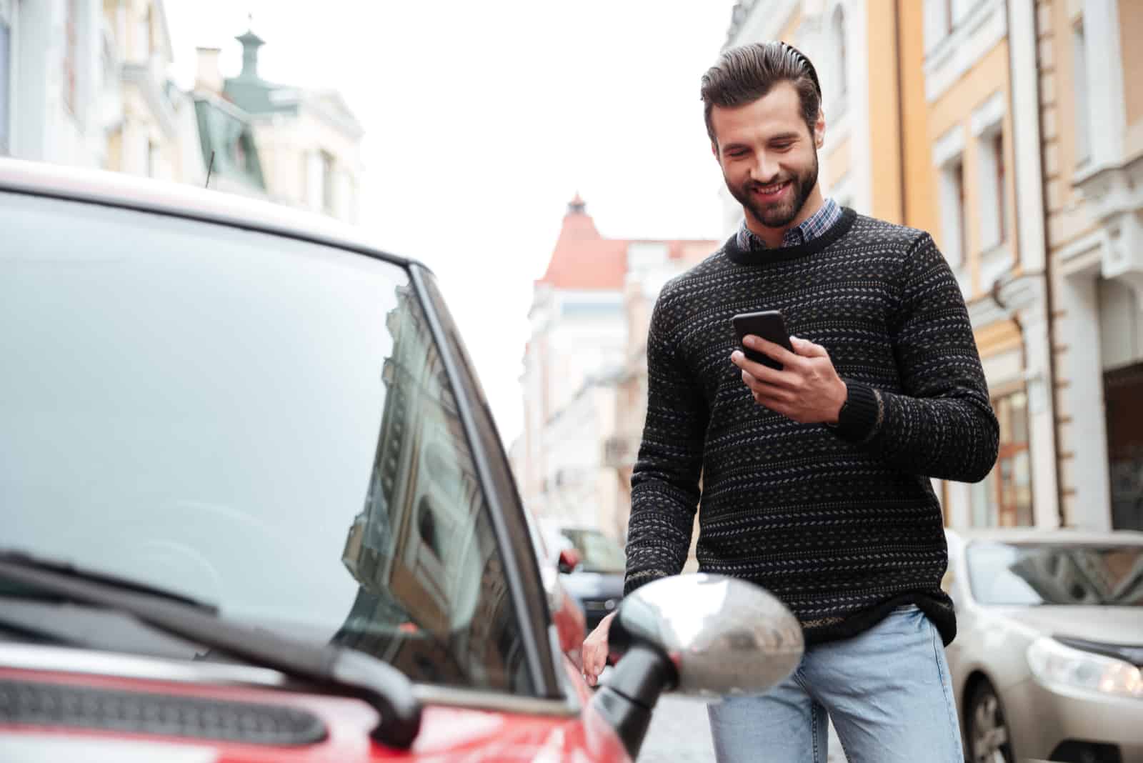 Un jeune homme souriant debout à côté d'une voiture et en appuyant sur un bouton du téléphone