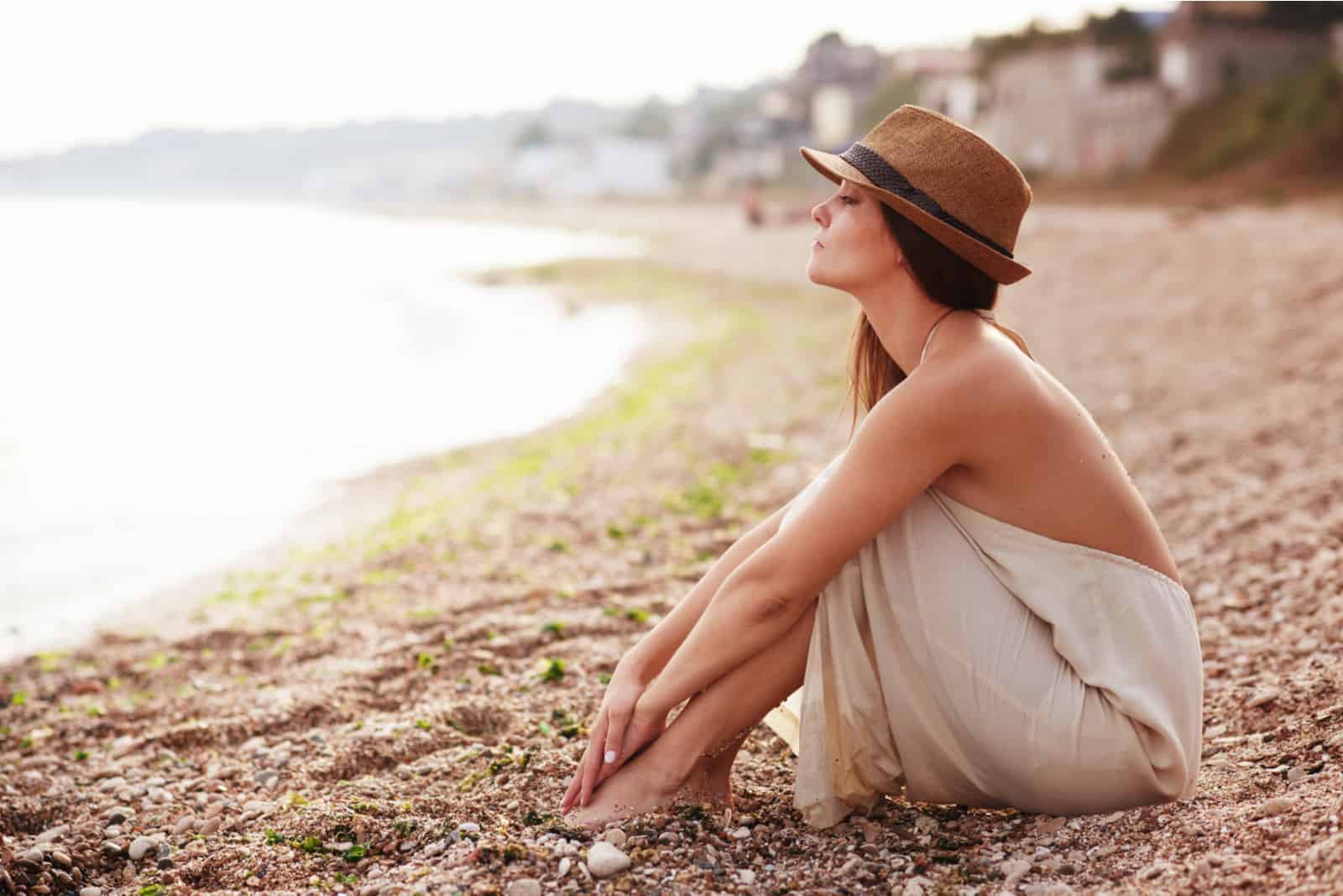 Une femme aux longs cheveux bruns avec un chapeau sur la tête est assise sur la plage